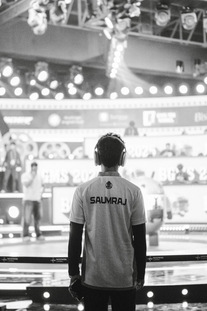 A professional gamer in headphones stands on stage at an exciting esports event.